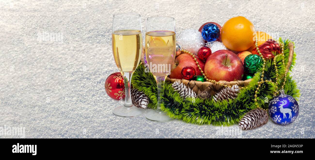 Noël encore la vie avec des verres de champagne un panier de fruits et de boules sur l'aspect granuleux de la neige fraîche. Décor d'hiver Décembre Banque D'Images