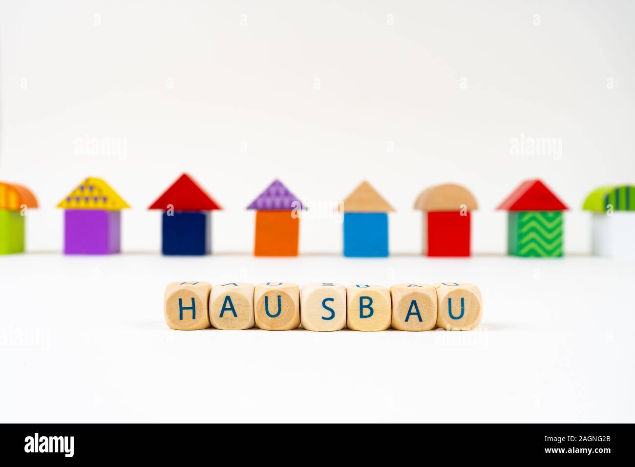 Bloc en bois avec des lettres pour dire 'Hausbau" (allemand pour la construction d'une maison) en face de maisons jouet coloré Banque D'Images