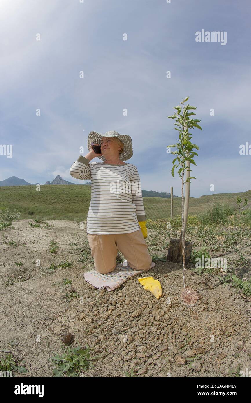 Femme âgée parle jardin plantation sur le téléphone Banque D'Images