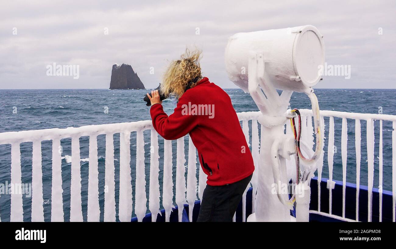 Un navire congelé en mer dans l'Antarctique, avec de la glace sur les grilles et un projecteur, tandis qu'une femme photographe prend des photos. Banque D'Images