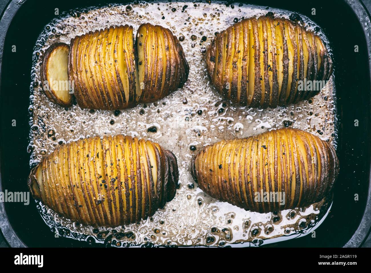 Hasselback Pommes de terre avec le beurre fondu, le sel et le poivre dans une rôtissoire, déposer le bac Banque D'Images