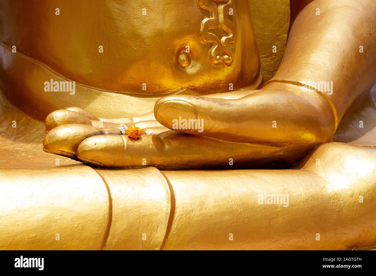 Main dorée de Bouddha dans un temple de Bangkok tenant une seule fleur comme offrande dans une main ouverte Banque D'Images