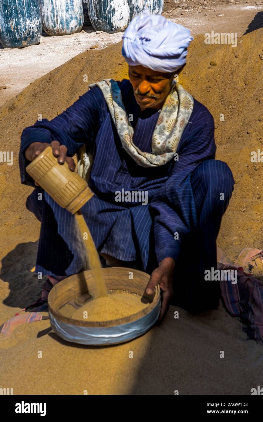 Novembre 2019, l'EGYPTE - homme musulman Egypte en vêtements traditionnels se verse dans le bol de sable, le temple de Louxor, Egypte Banque D'Images