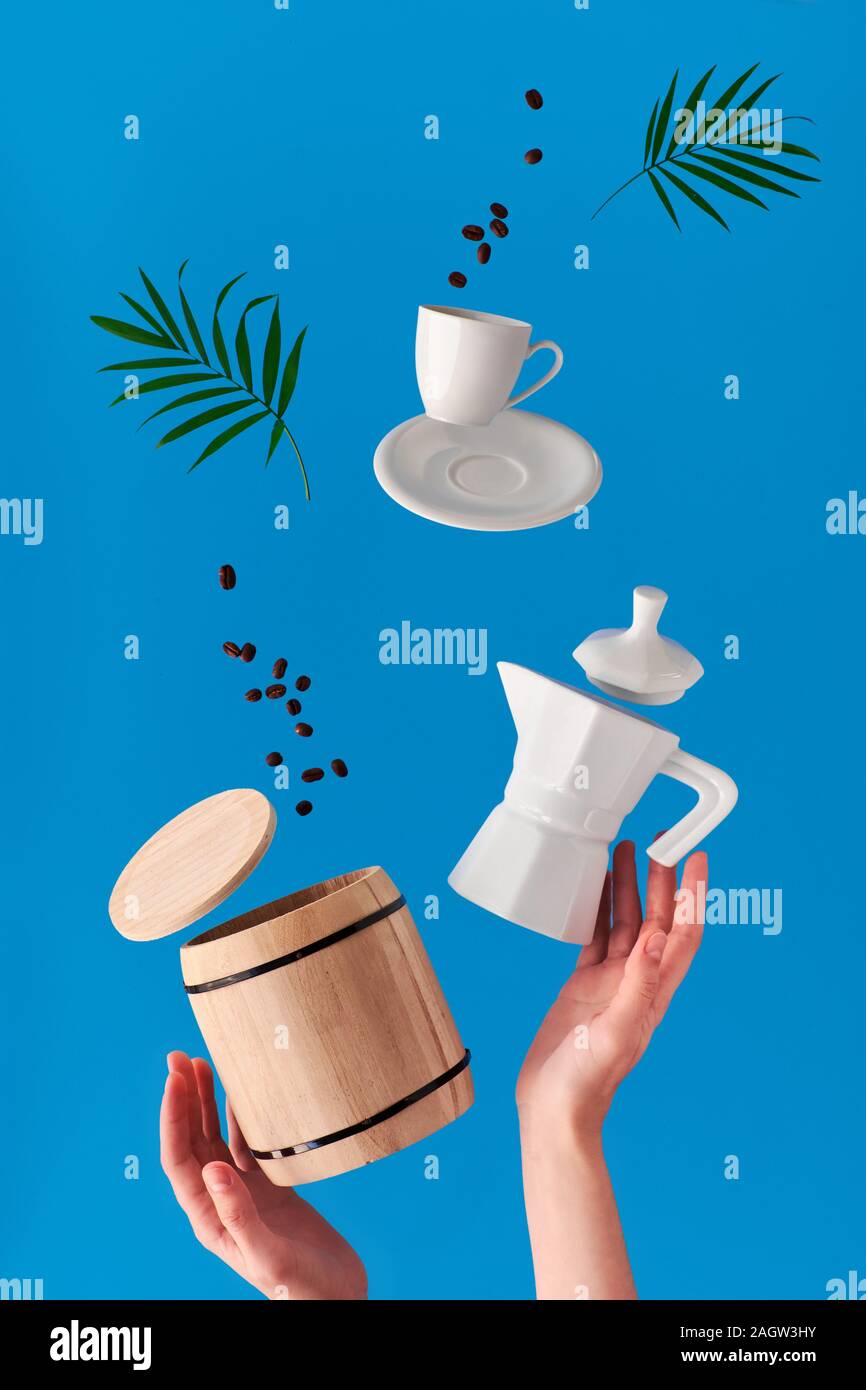 La lévitation à la mode. La ligne de vol de grains de café entre la céramique cafetière et tasse à expresso avec soucoupe. Arrière-plan de menthe bleue avec palm naturel laisser Banque D'Images