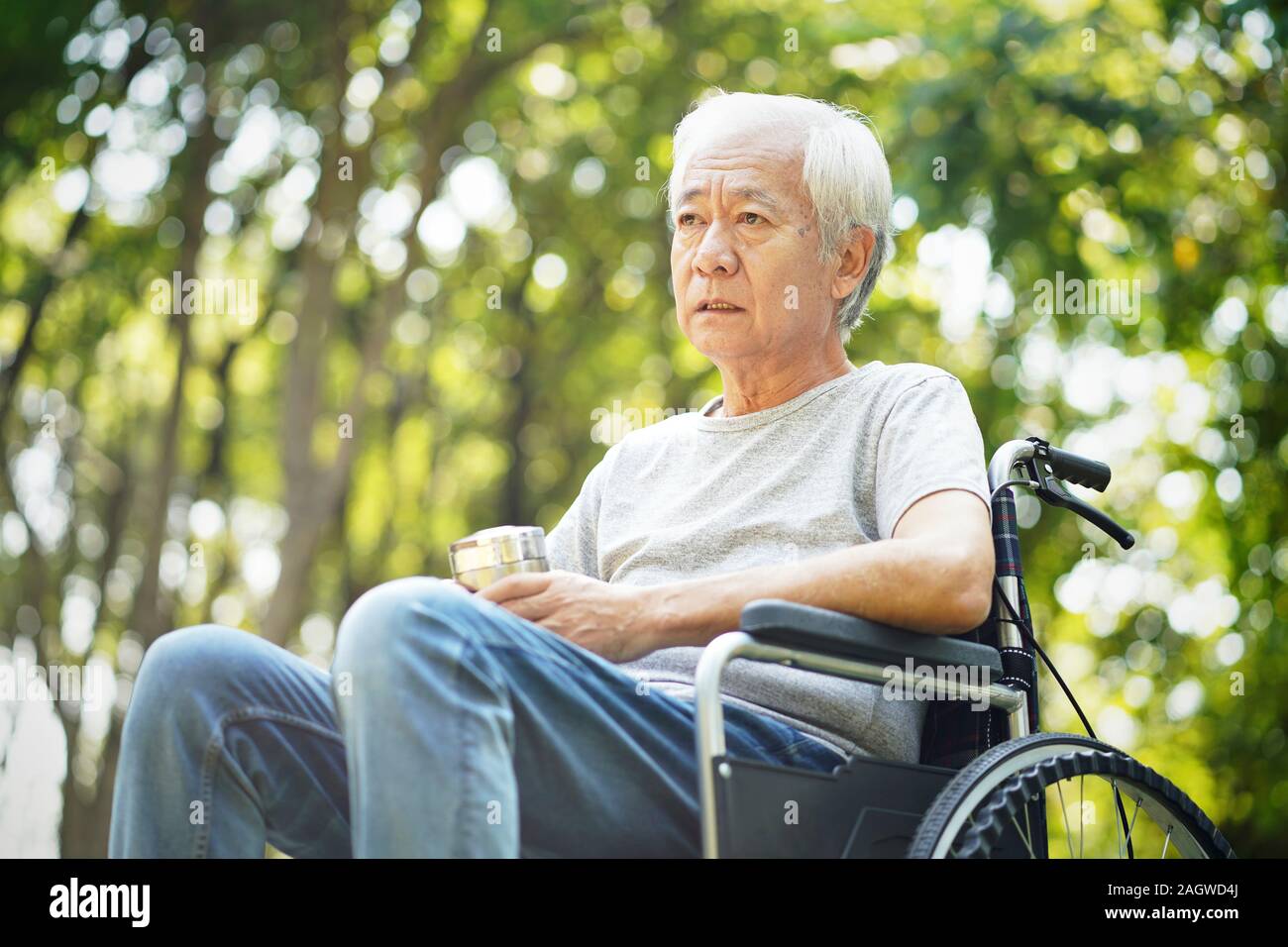 Triste homme asiatique assis en fauteuil roulant à l'extérieur Banque D'Images