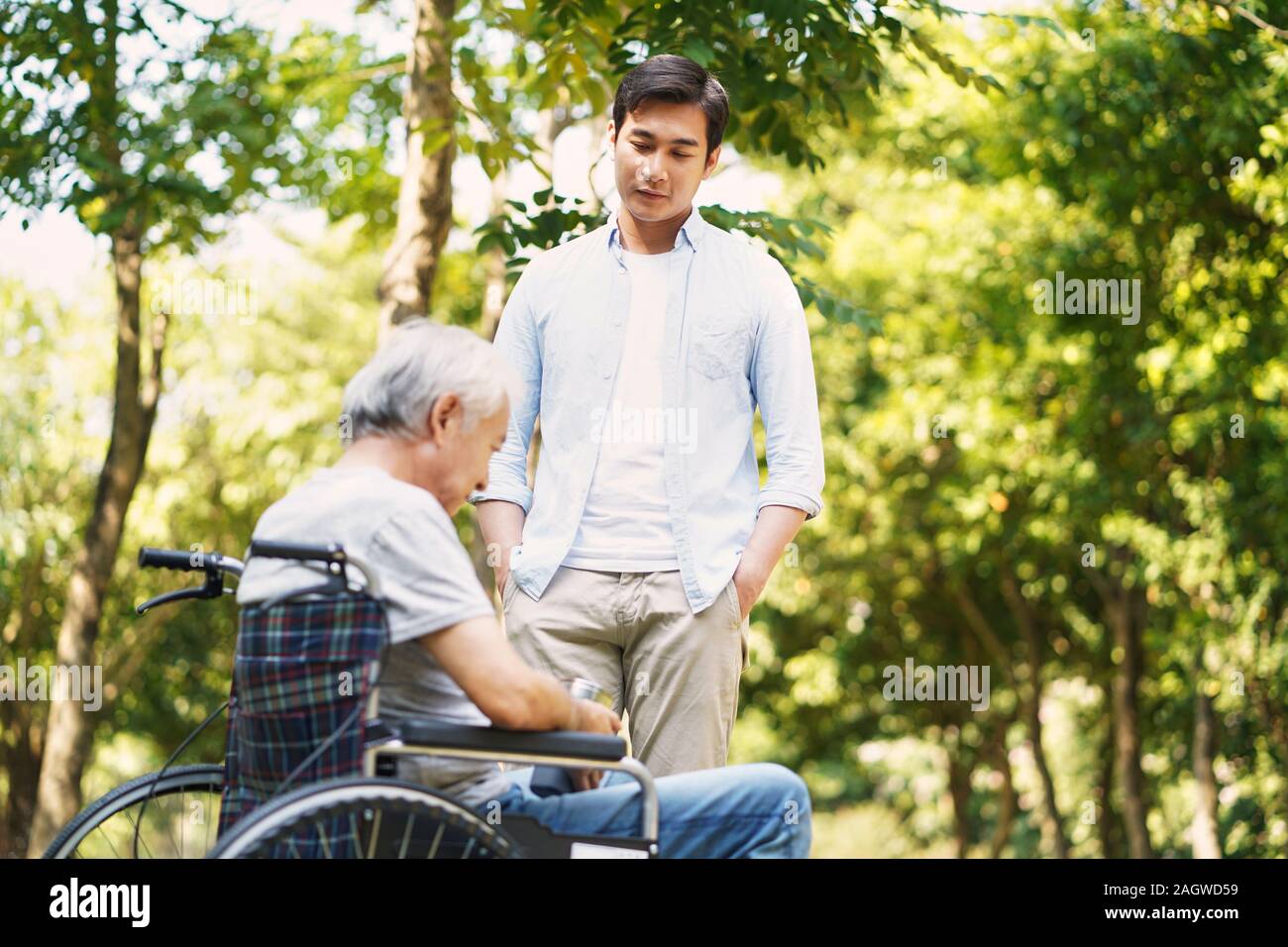 Les jeunes adultes asiatiques fils discutant avec fauteuil roulant lié à l'extérieur du parc en père déprimé Banque D'Images