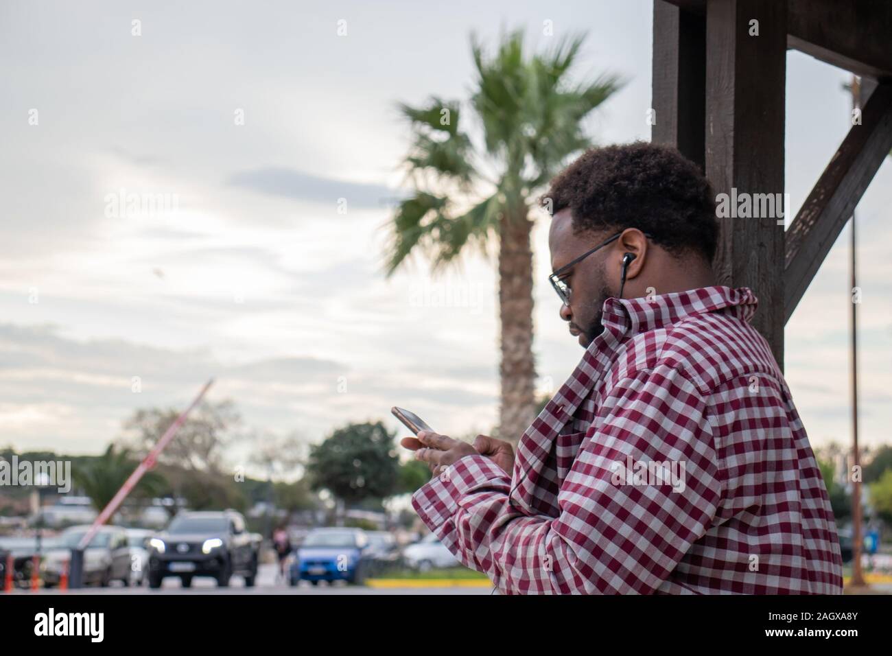 Athènes, Grèce - 30 novembre 2019 : South American man looking at le téléphone en été contre le palmier avec des écouteurs Banque D'Images
