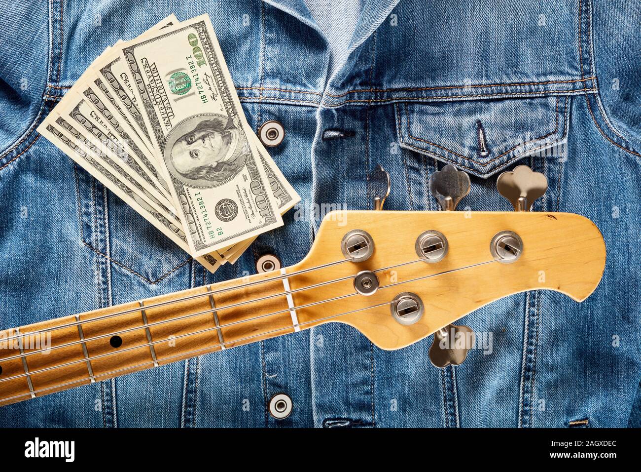 Tête de guitare basse et d'une centaine de dollars sur le denim jeans veste. Concept de faire ou gagner de l'argent dans l'industrie de la musique. Banque D'Images