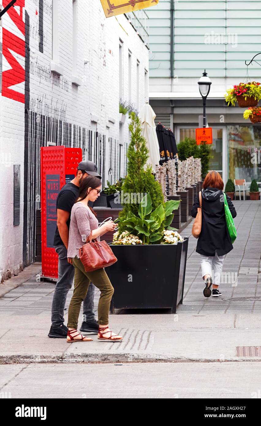 Montréal, Canada - Juin 2018 : Jeune couple canadien marche sur la rue et à la recherche à leur smartphone à Montréal, Canada. Banque D'Images