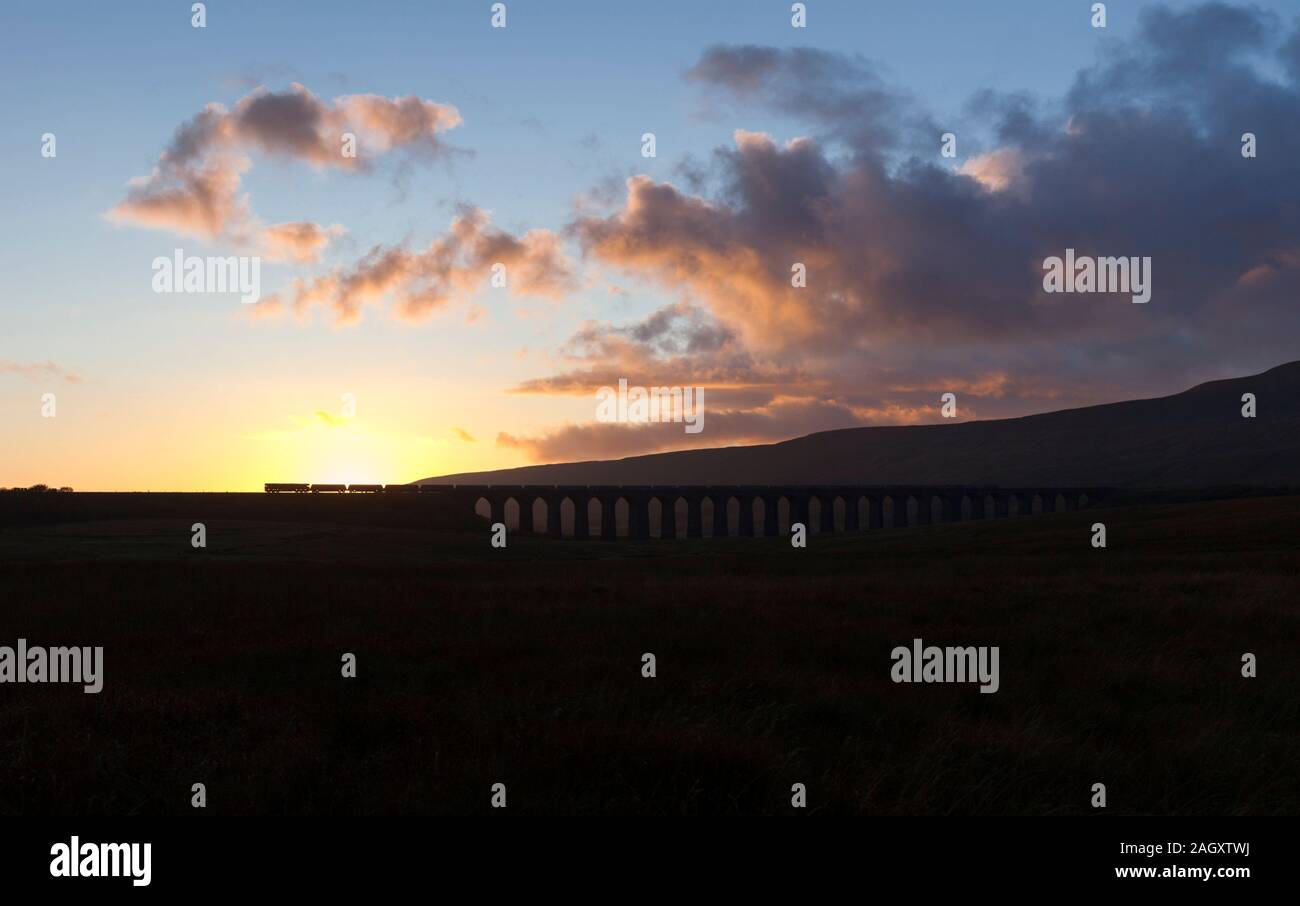 GB Railfreight locomotive classe 66 viaduc Ribblehead passage au coucher du soleil faire une silhouette avec un train de marchandises transportant des granulats Banque D'Images