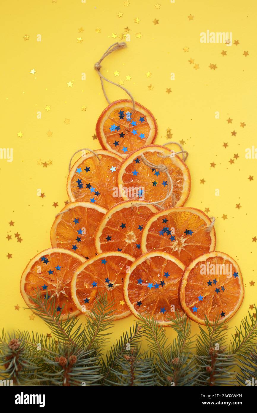 Dix tranches d'orange séchée avec des cordes, imitant de noël avec des branches d'arbres de pin et glitter bleu sur fond jaune Banque D'Images