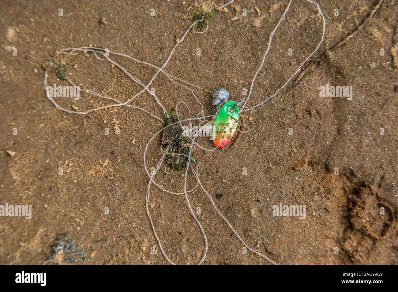 Un leurre de pêche portant sur la plage de la rivière dans le sable avec un poids de plomb et le crochet sur le filament empêtré lors d'une journée ensoleillée en été Banque D'Images