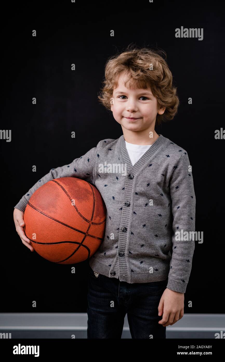 Adorable petit garçon dans casualwear holding ball pour jouer au basket-ball Banque D'Images