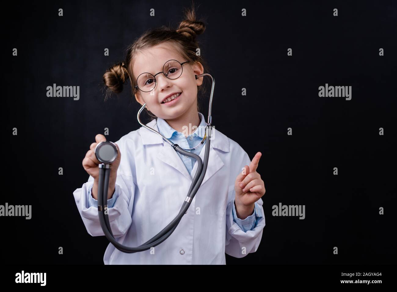 Petite fille joyeuse dans l'aide de blanchons stéthoscope en pointant sur vous Banque D'Images