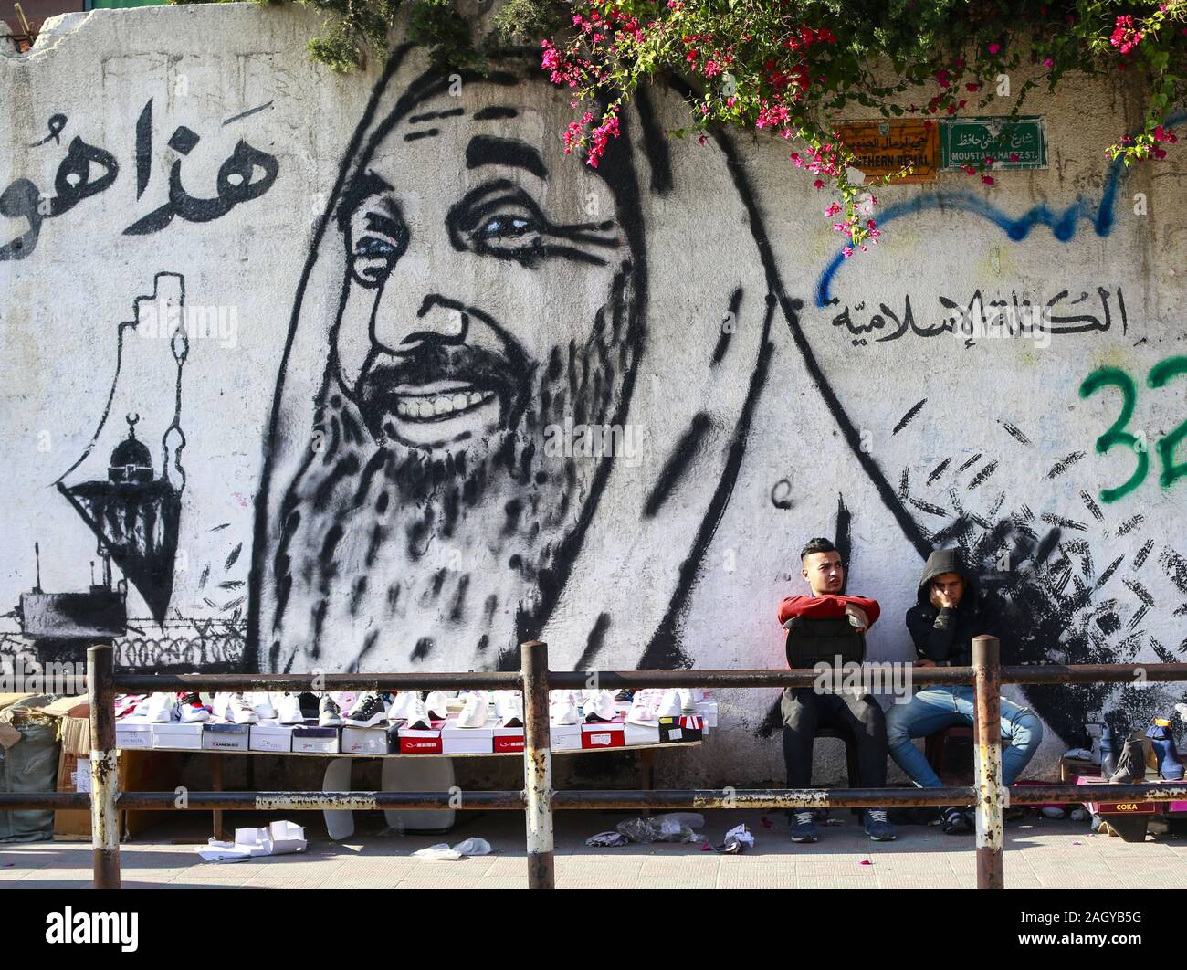 La ville de Gaza, la bande de Gaza, en Palestine. Dec 22, 2019. Les Palestiniens s'asseoir derrière une fresque murale représentant le chef spirituel du Hamas, cheikh Ahmed Yassine et Abdel Aziz Rantisi leader dans la ville de Gaza. Credit : Mahmoud Issa/Quds Net News Wire/ZUMA/Alamy Live News Banque D'Images