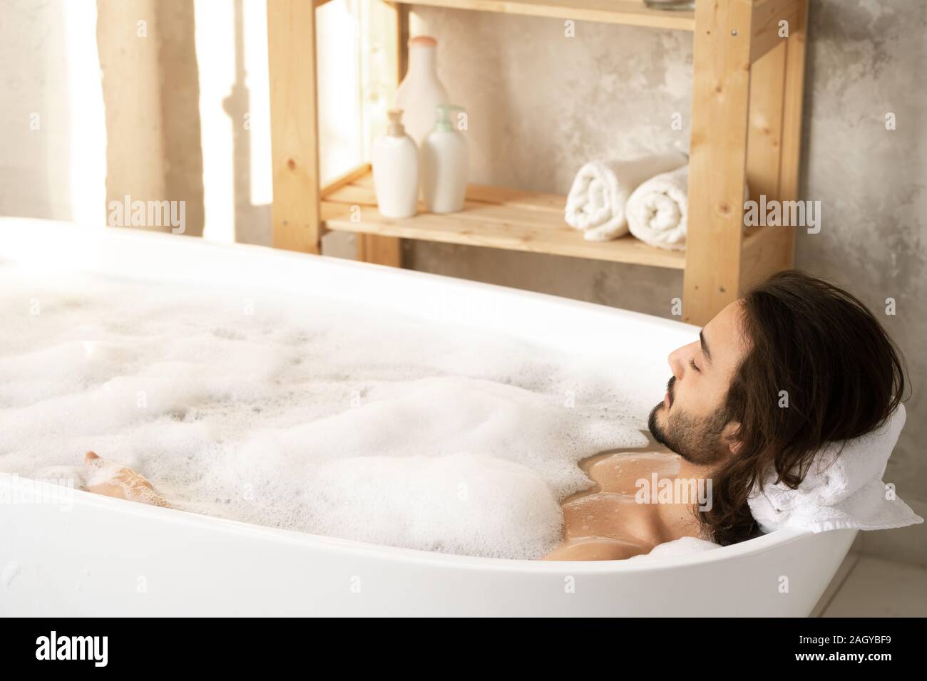 Jeune homme détendu enjoying bath avec mousse tout en mettant sa tête sur les sèche-serviettes Banque D'Images