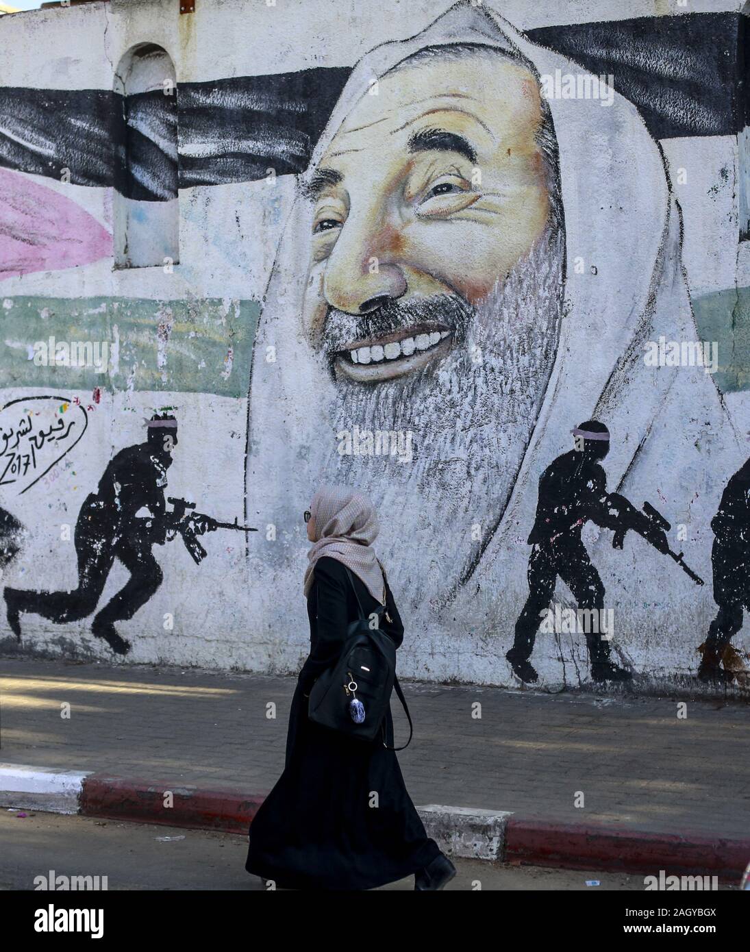 La ville de Gaza, la bande de Gaza, en Palestine. Dec 22, 2019. Une femme palestinienne passe devant une peinture murale représentant le chef spirituel du Hamas, cheikh Ahmed Yassine, et un chasseur masqué des Brigades Al-Qassam, la branche armée du Hamas, à Gaza. Credit : Mahmoud Issa/Quds Net News Wire/ZUMA/Alamy Live News Banque D'Images