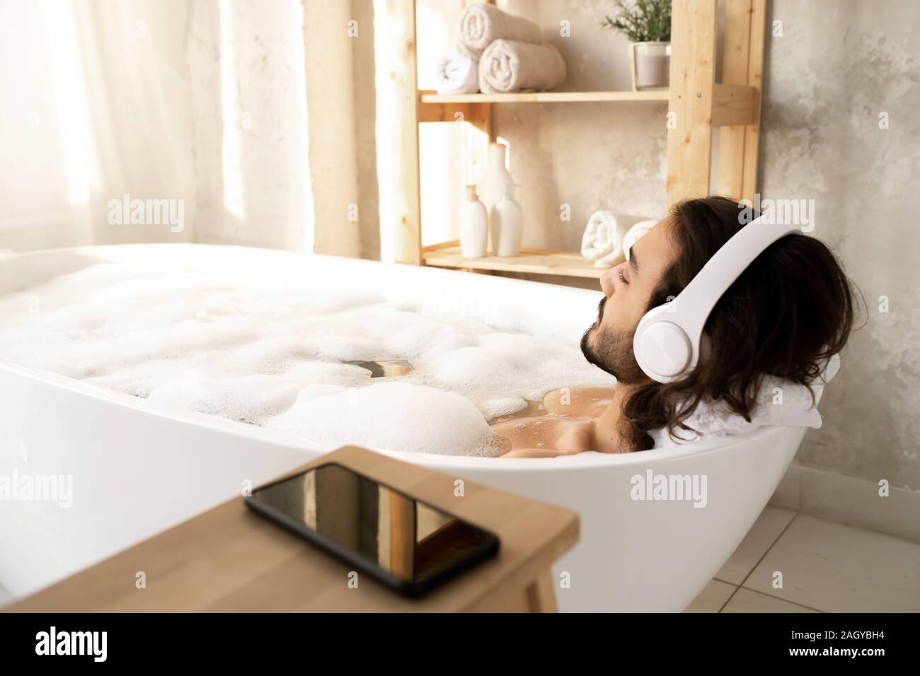 Jeune homme avec un casque blanc couché dans une baignoire remplie d'eau  chaude et la mousse Photo Stock - Alamy