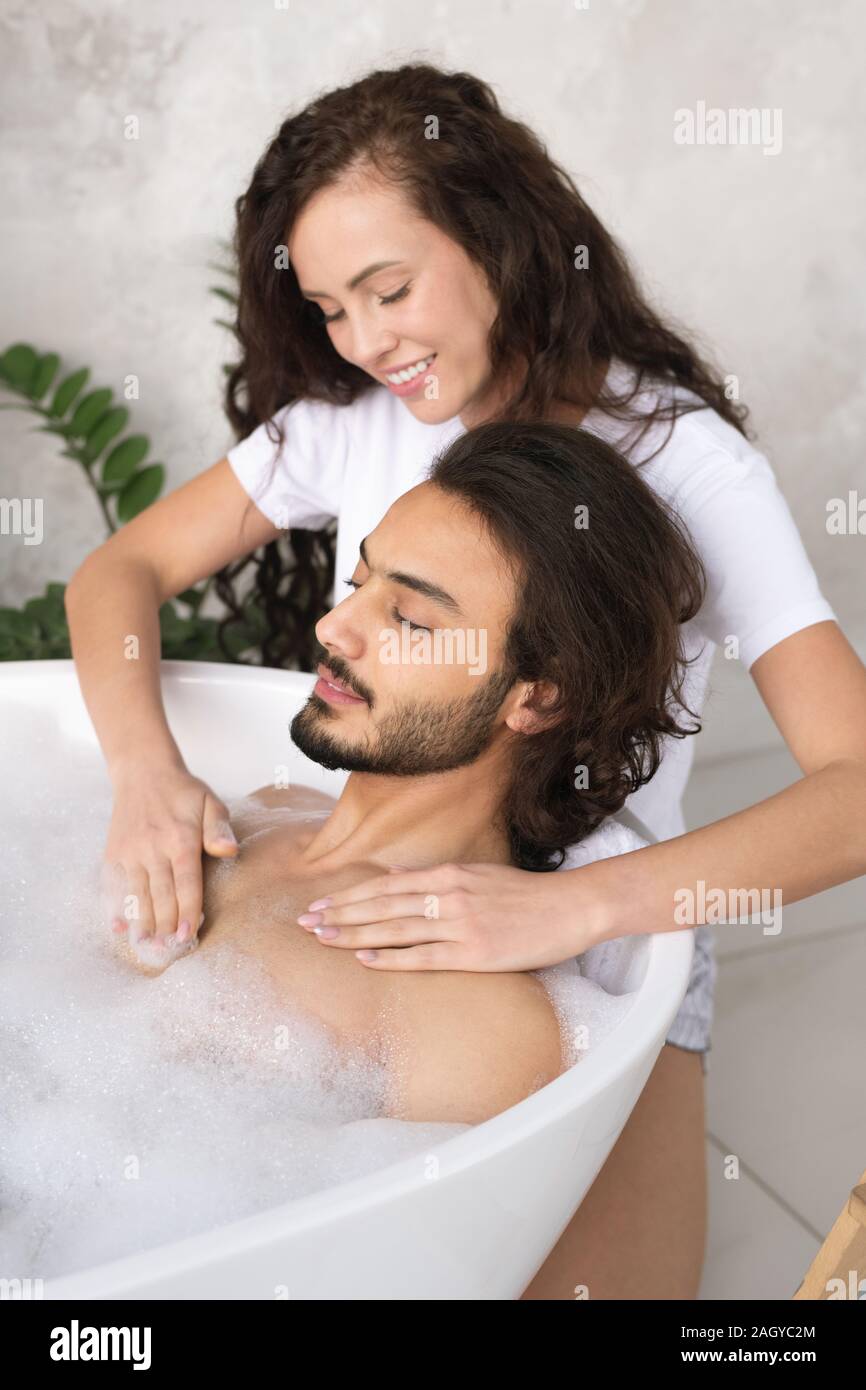 Young smiling woman making massage de la poitrine de son mari dans la baignoire relaxante Banque D'Images