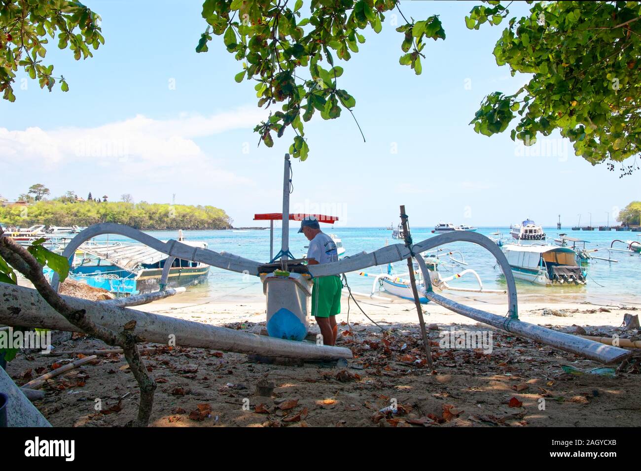 Angler se tenir derrière dans la couronne de l'arbre d'ombre, de travailler sur son bateau à Bali beach Banque D'Images