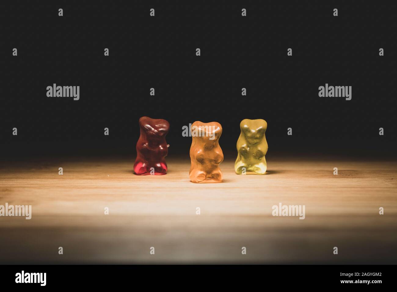 Un portrait de trois ours gummi de couleur différente, le bonbon est debout sur une planche en bois avec un éclairage qui dirait qu'ils sont sur une scène. Banque D'Images
