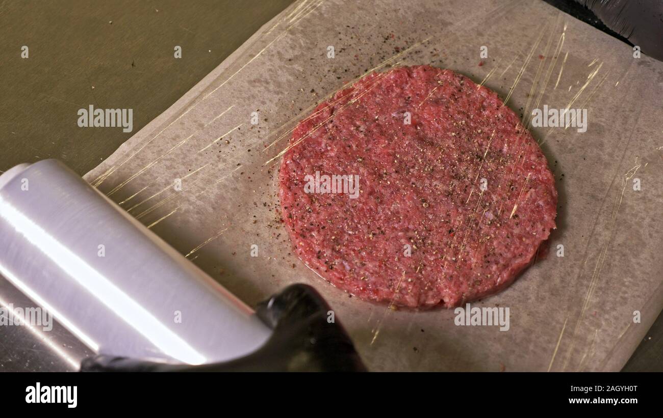 Faire cuire les médaillons de viande fait pour les hamburgers. Chef en noir gants alimentaire rend escalope. Les escalopes sont de niveau dans l'anneau d'acier dans un même médaillon. Banque D'Images