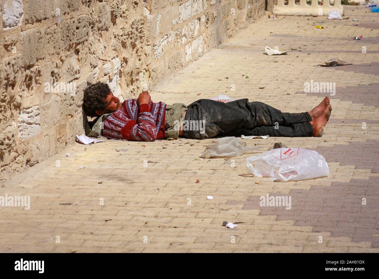 Un homme sans abri pieds nus, situé dans la rue au milieu des détritus de Monastir, en Tunisie Banque D'Images