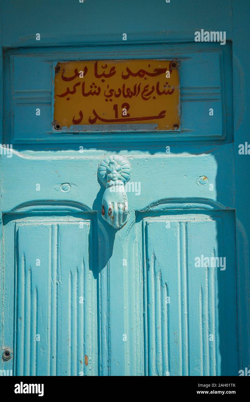 Porte bleue en partie au soleil et en partie à l'ombre avec l'étiquette jaune et l'écriture rouge à Hergla, Tunisie Banque D'Images