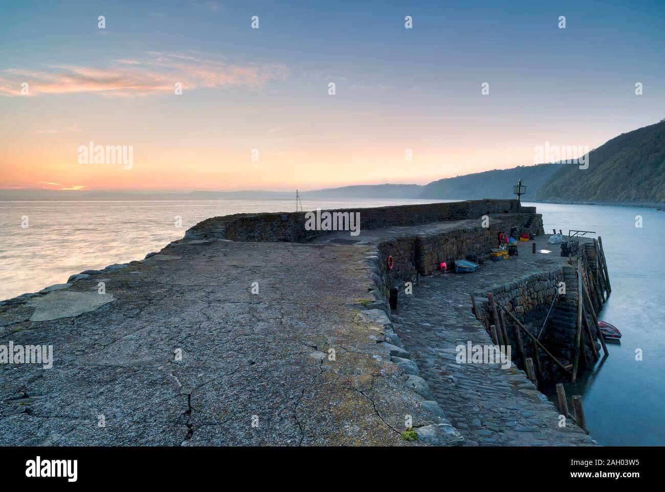 Port de Clovelly en début de matinée avec le soleil levant à l'horizon et un bateau de pêche qui navigue dans ce village de pêcheurs, North Devon, South West, Banque D'Images