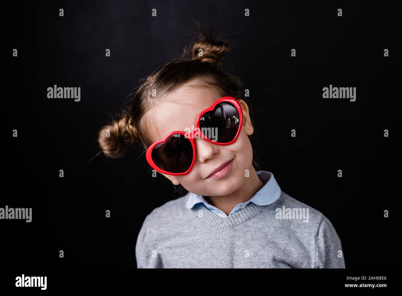 Jolie fille à lunettes avec lentilles élégant heartshaped debout en face de la caméra de manière isolée sur fond noir Banque D'Images