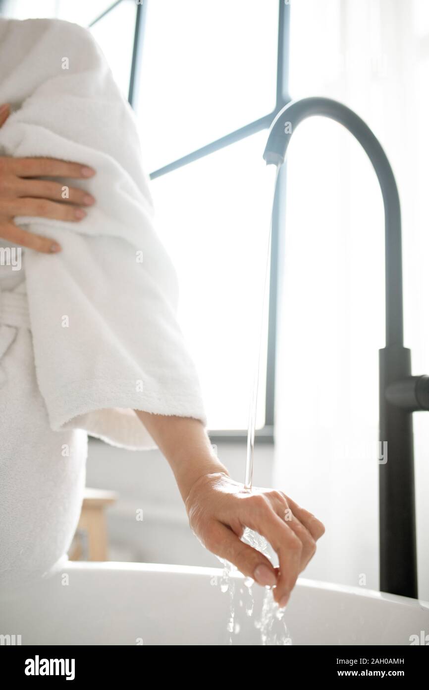 Main de jeune femme contrôle de température de l'eau découlant de puiser dans une baignoire Banque D'Images