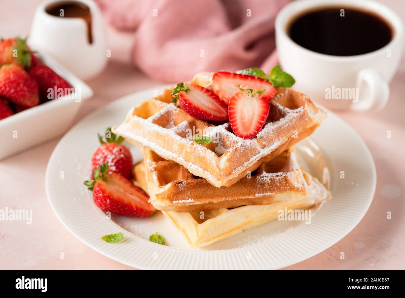 Gaufres Belges avec fraises et tasse de café noir sur fond rose. Délicieux petit-déjeuner sucré de la nourriture. Riche en glucides et sucre, des aliments insalubres ea Banque D'Images