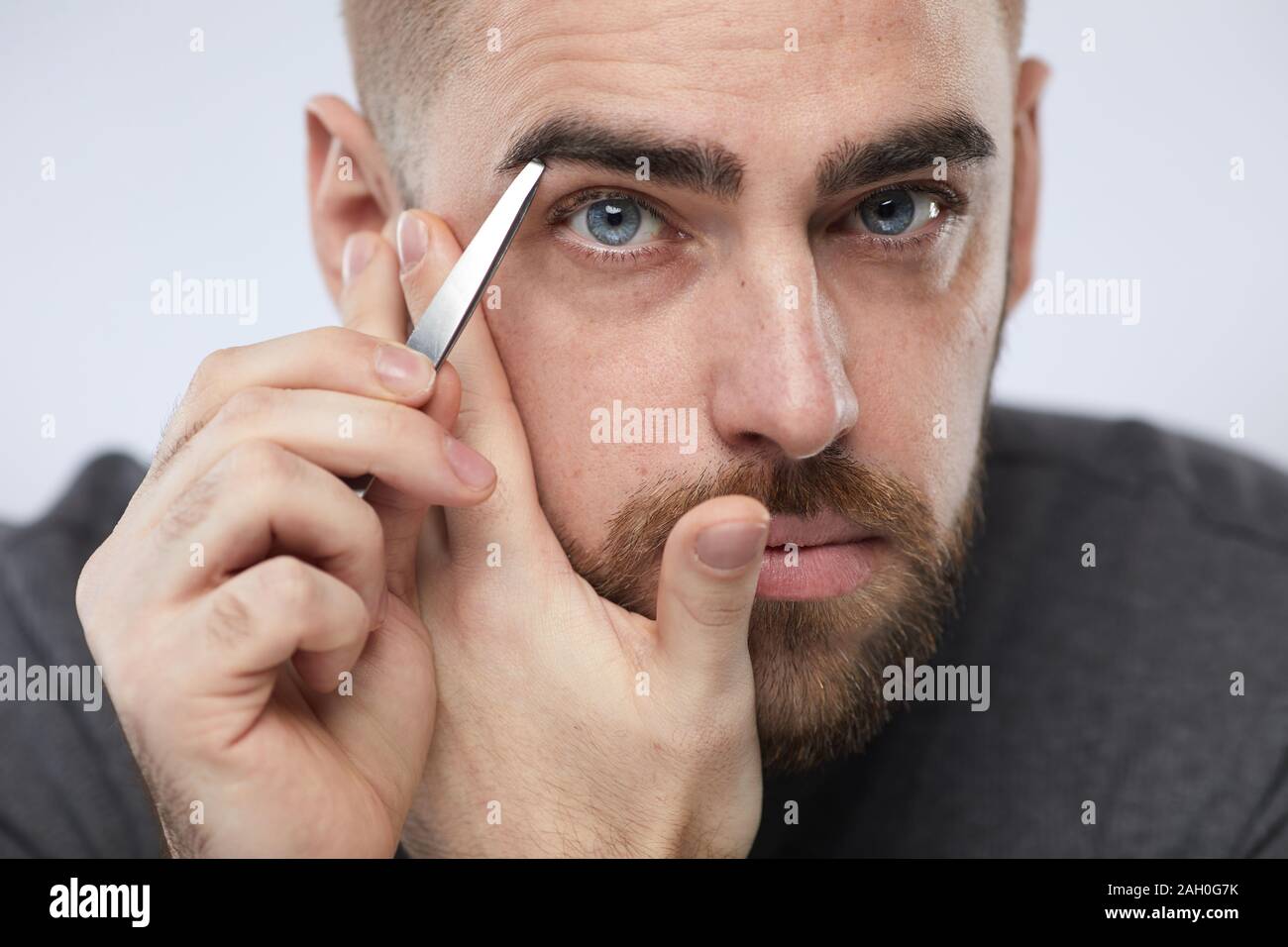 Close up portrait of Horizontal beau jeune homme tweezing ses sourcils looking at camera Banque D'Images