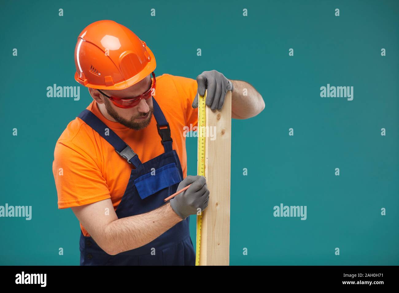 Portrait studio horizontal de carpenter wearing orange et bleu taille uniforme planche en bois, fond bleu turquoise Banque D'Images