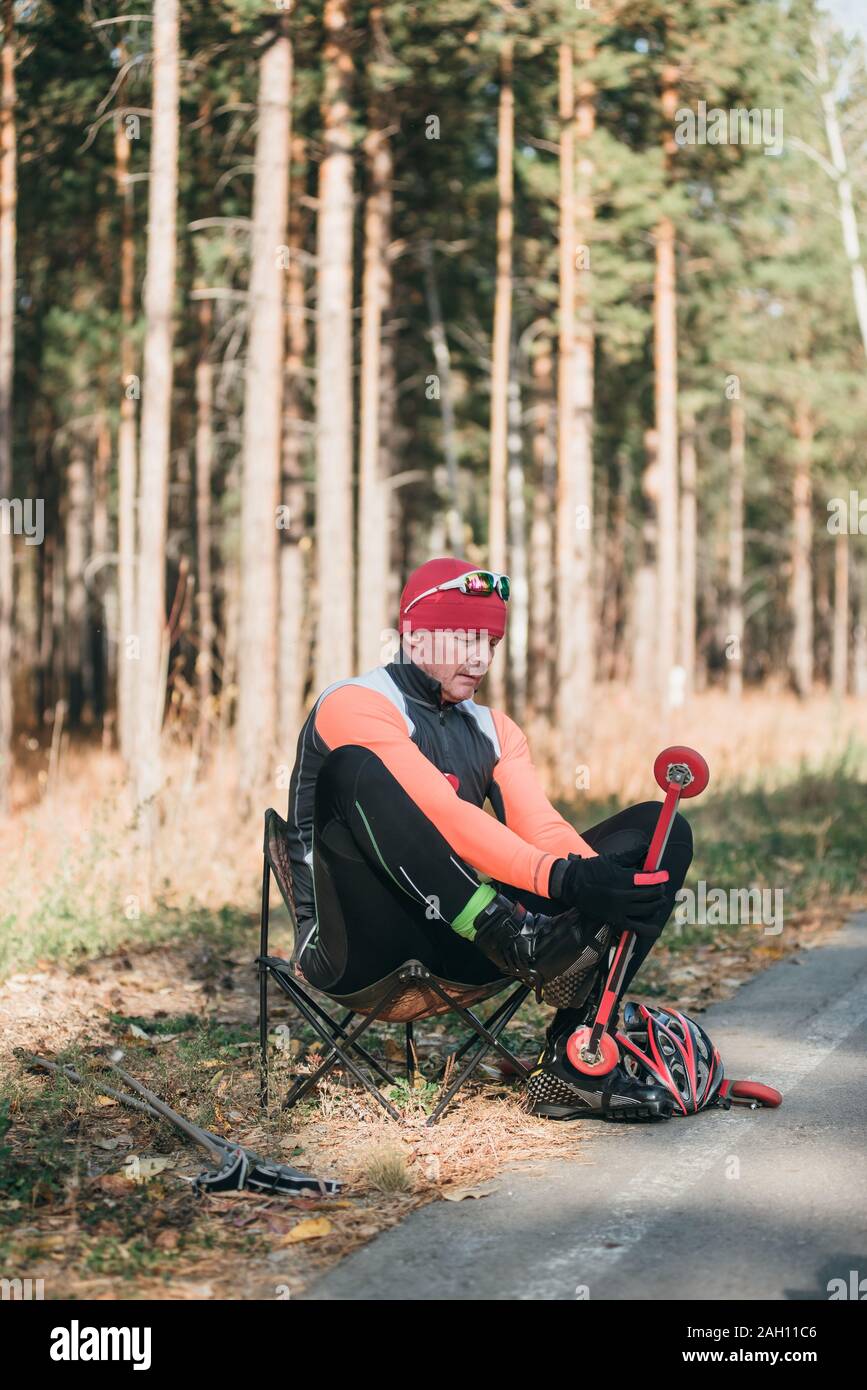 Un athlète, à la formation de patins à roulettes. Le Biathlon tour sur les skis à roulettes avec des bâtons de ski, dans le casque. L'athlète est prêt à démarrer. L'automne Banque D'Images