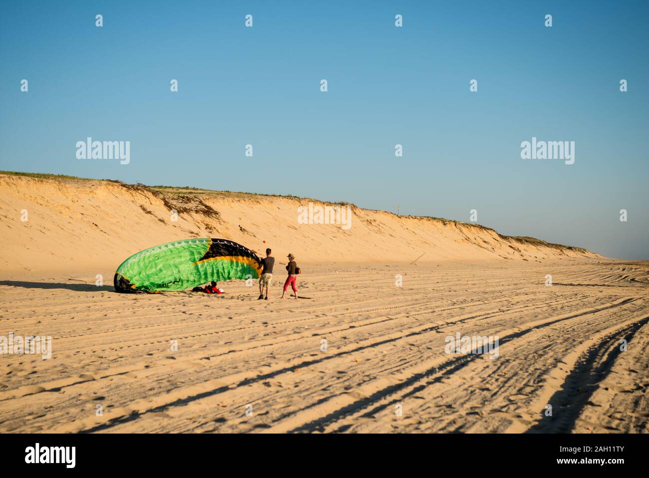 Parapentiste prépare à lancer sur une plage remplie de traces de pneu dans le soleil du soir Banque D'Images