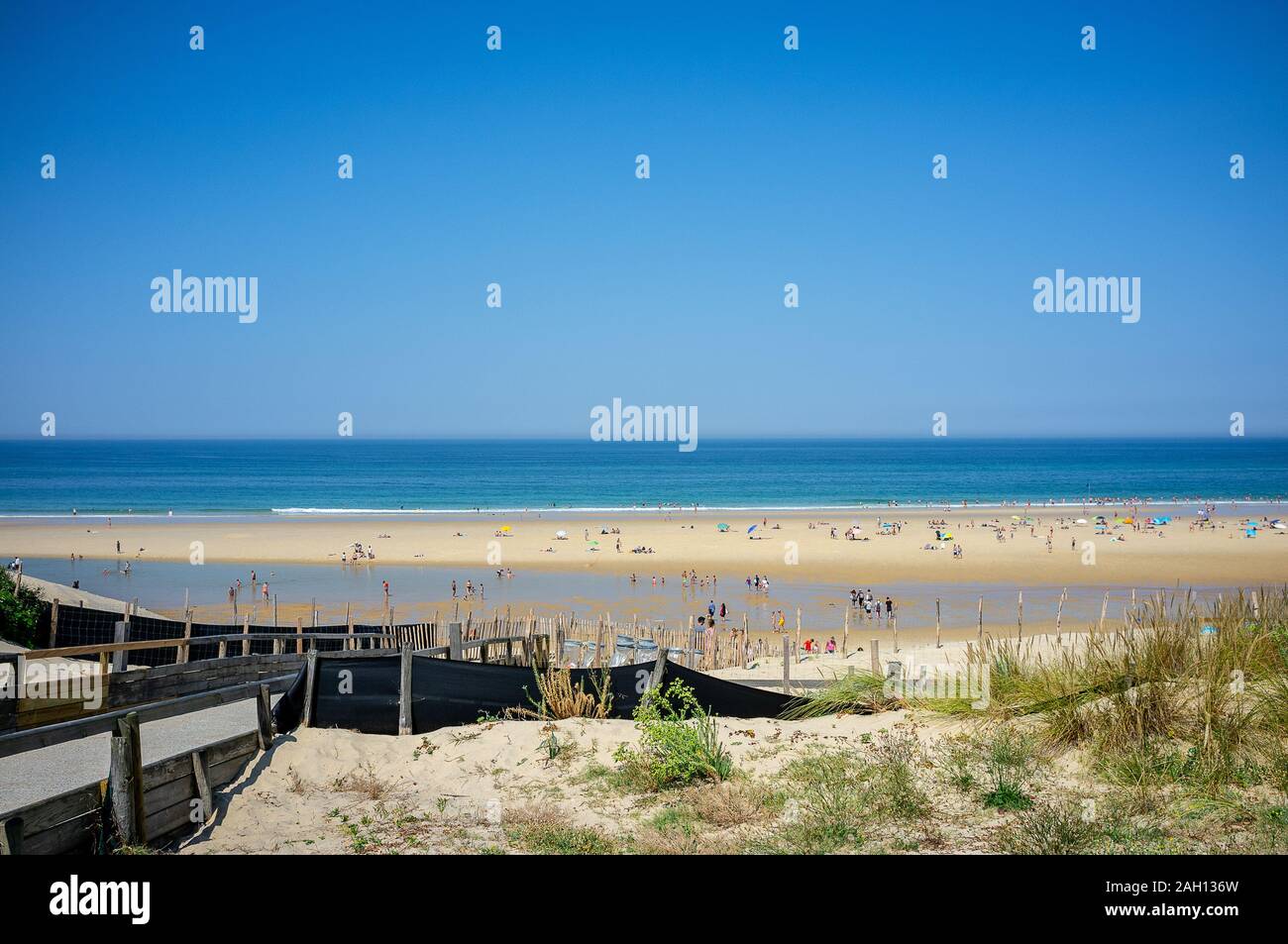 Acier bleu ciel au-dessus d'une plage bondée à bleu océan atlantique en france avec sol en bois clôture en premier plan Banque D'Images