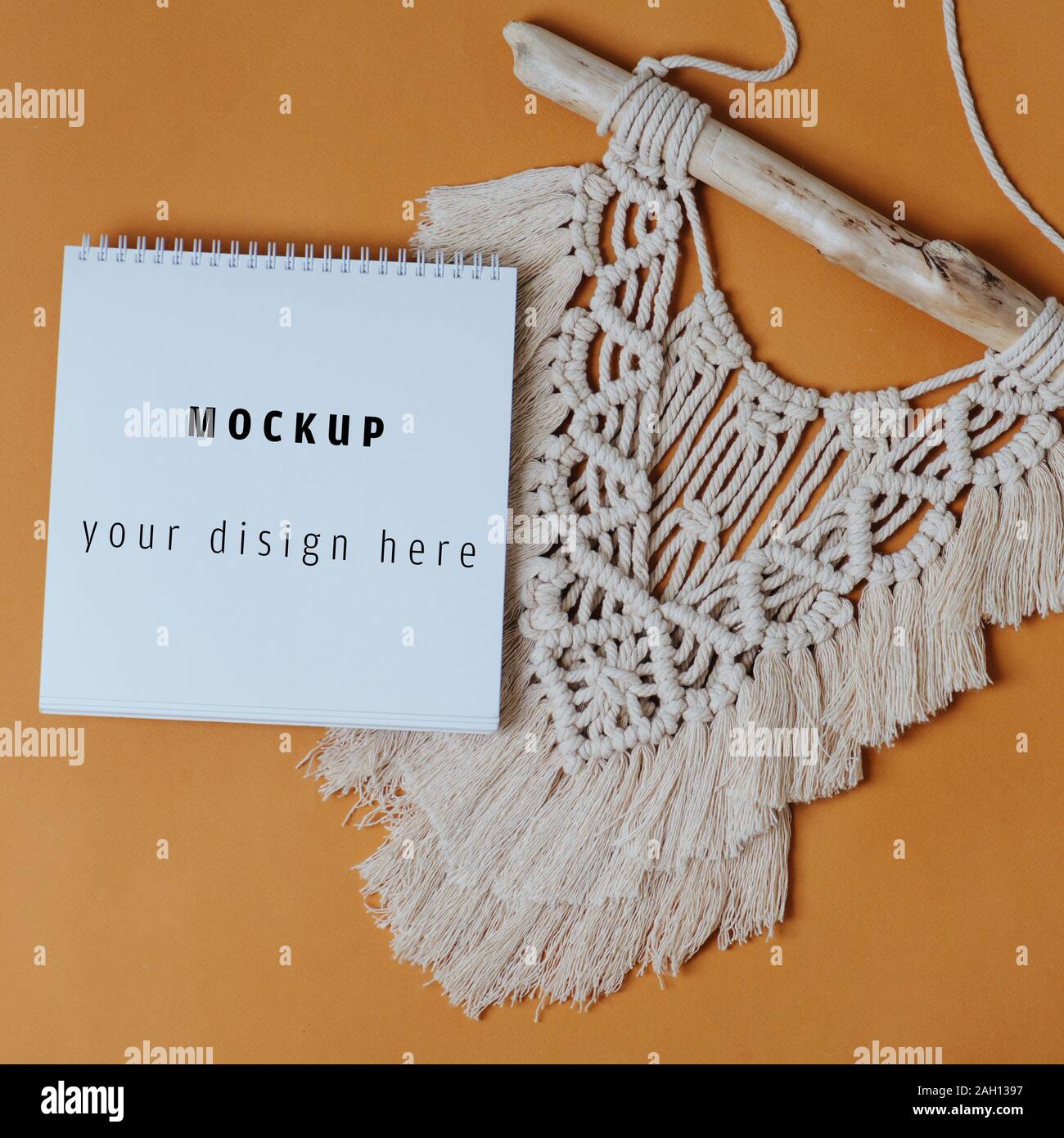 Mokeup carnet à spirales sur macrame tapisserie close up sur fond orange Banque D'Images
