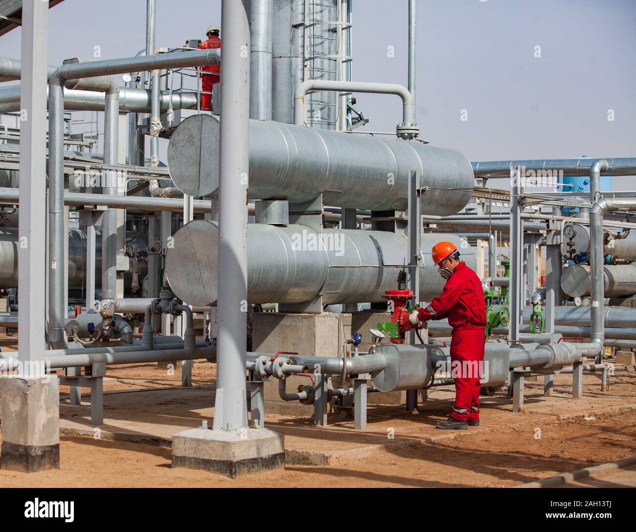 Travailleur en vêtements de travail rouge et orange casque et un masque à gaz de raffinerie de pétrole et de gaz dans l'usine un désert. Banque D'Images