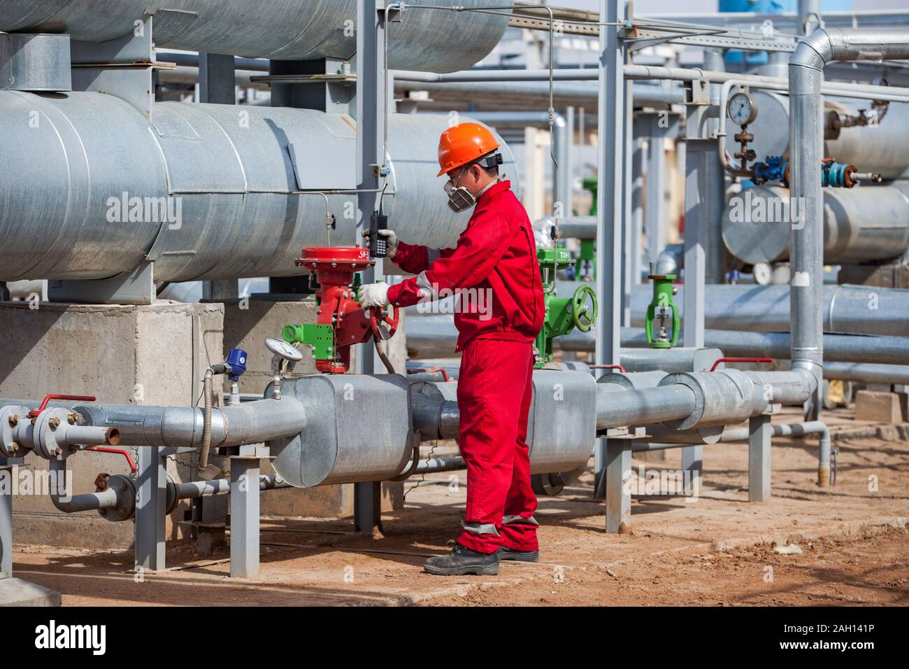 Travailleur en masque à gaz et des vêtements de travail rouge et orange casque de travail sur le pétrole et le gaz raffinerie dans un désert.. Banque D'Images