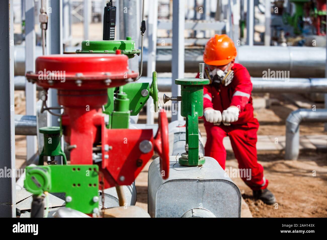 Travailleur en worwear rouge et masque à gaz et d'huile d'orange casque sur la raffinerie. L'accent sur le premier plan. Banque D'Images