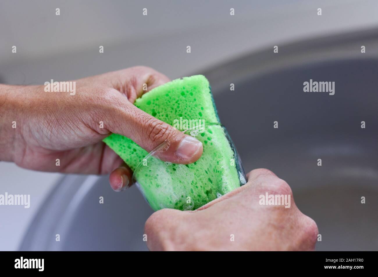 Libre d'un jeune homme de race blanche lave un verre dans un évier de cuisine avec une éponge verte Banque D'Images