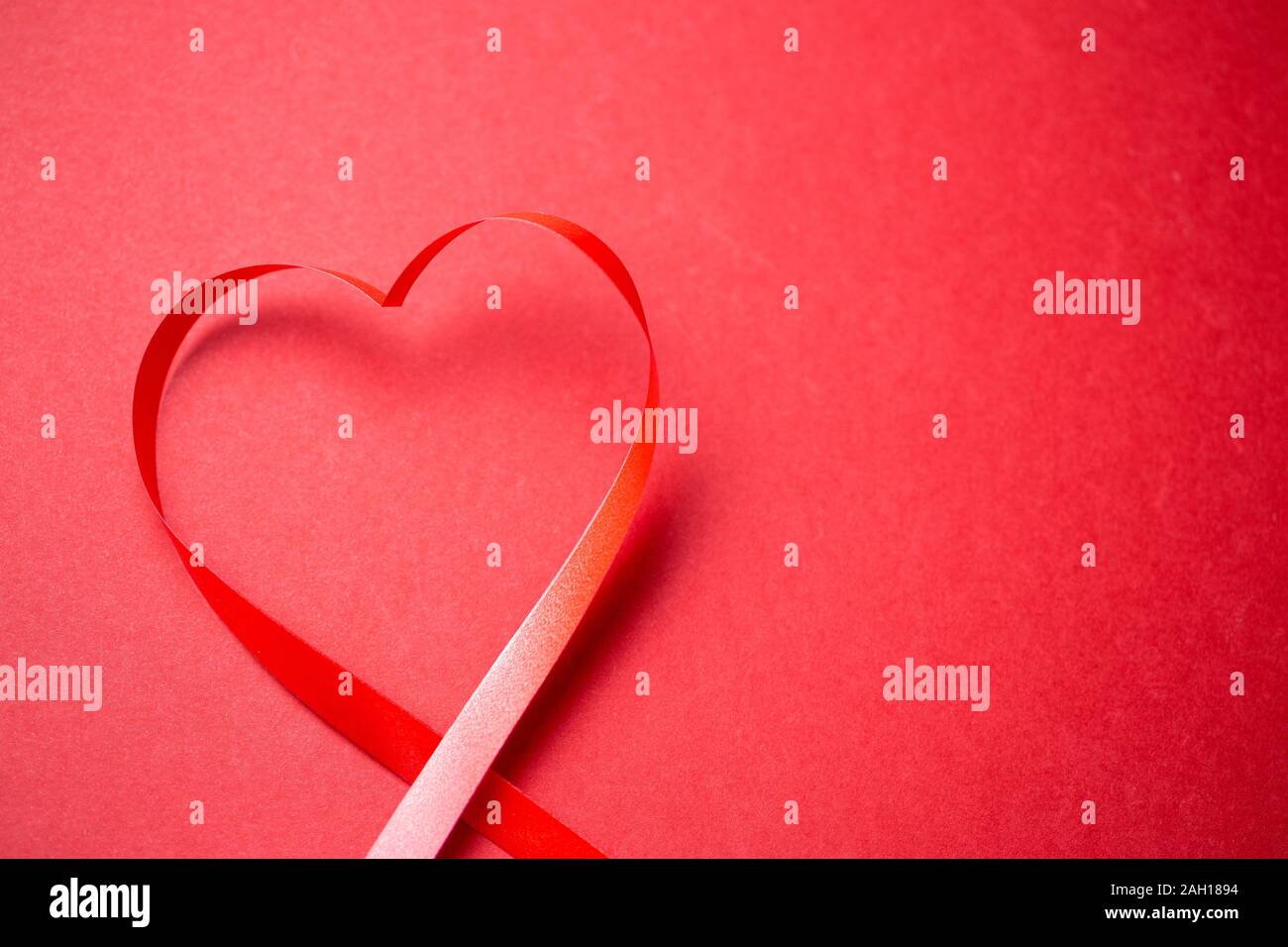 Coeur fait de cadeau rouge bow sur fond rouge. Carte greating minimaliste avec place pour le texte Banque D'Images