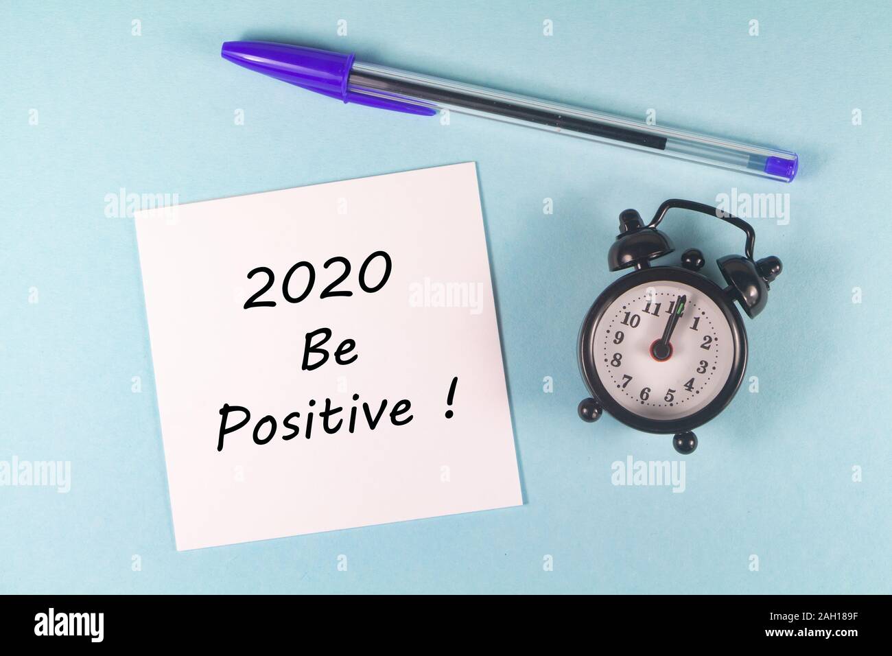 Stylo, papier avec 2020 être positif et réveil noir sur fond bleu Banque D'Images
