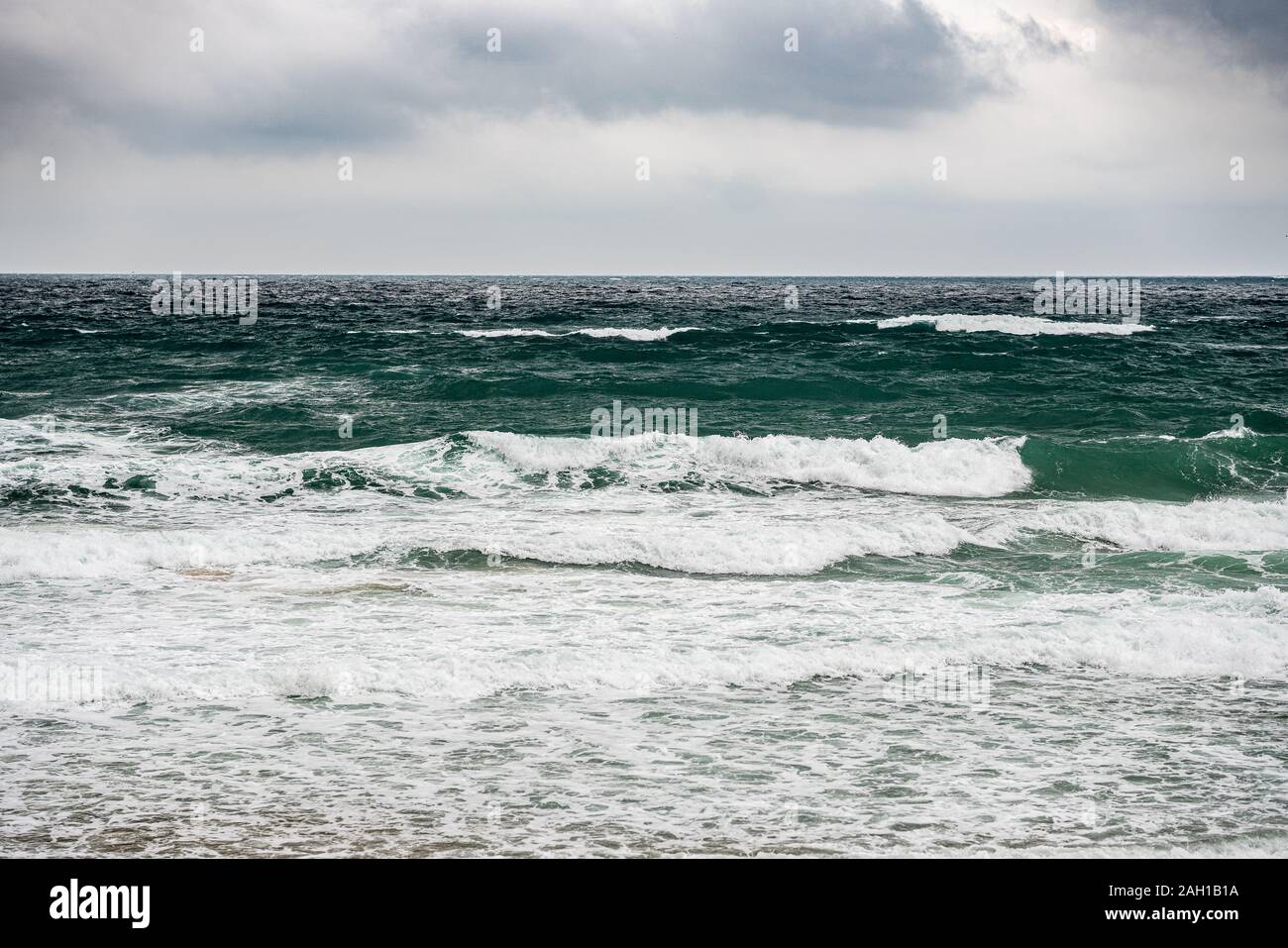 L'état de la mer et les vagues se briser en de plage et les rochers sur le premier plan, les surfers dans l'arrière-plan Banque D'Images
