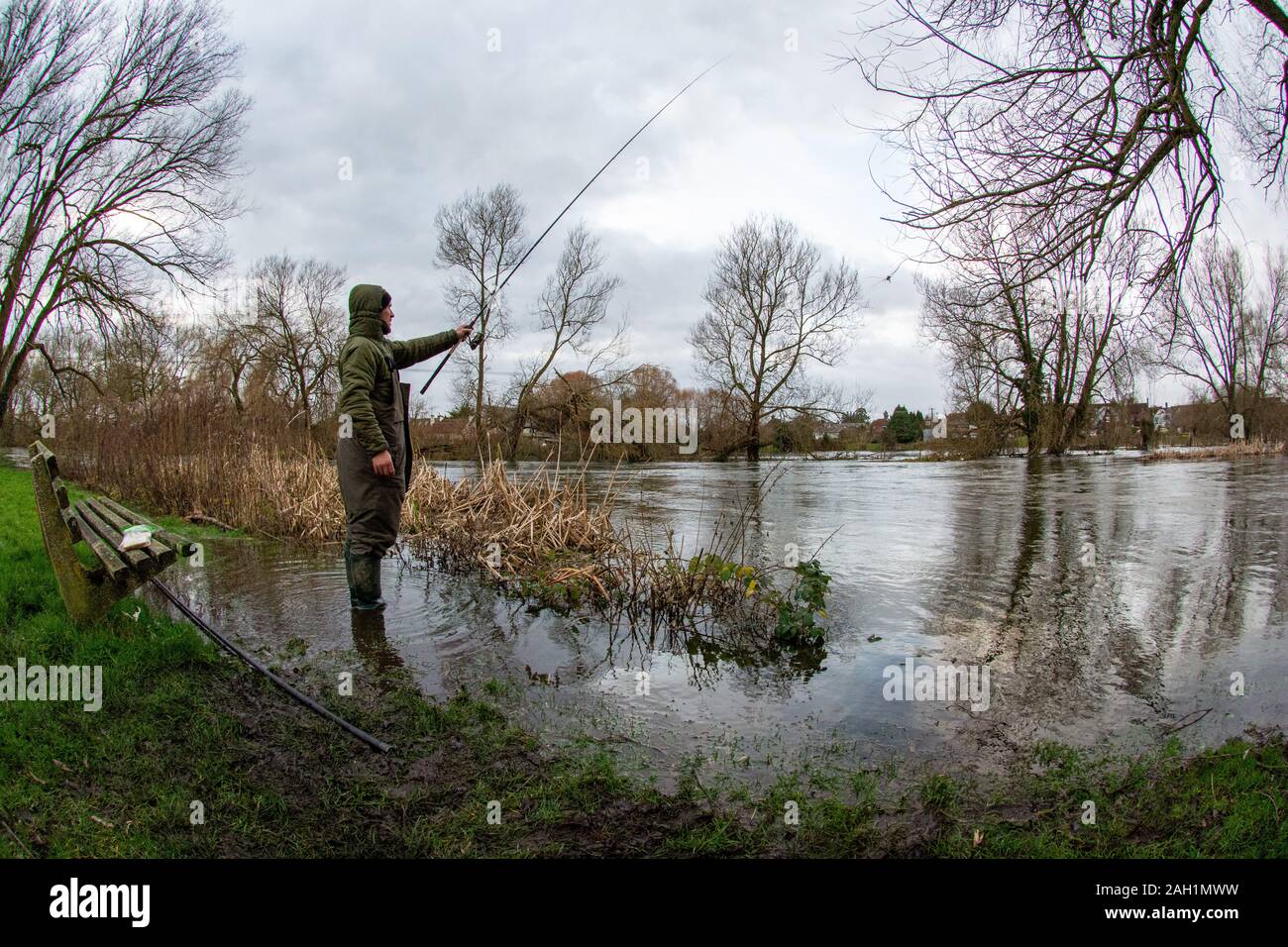 Pêcheur jetant une ligne avec une canne à pêche sur la rive d'une rivière pleine à éclater après de fortes pluies récentes. Une alerte d'inondation a été augmentée à une alerte d'inondation le long de cette section de la rivière Avon alors que les niveaux d'eau souterraine continuent d'augmenter. Fordingbridge, New Forest, Hampshire, Royaume-Uni, 23 décembre 2019, météo. Banque D'Images