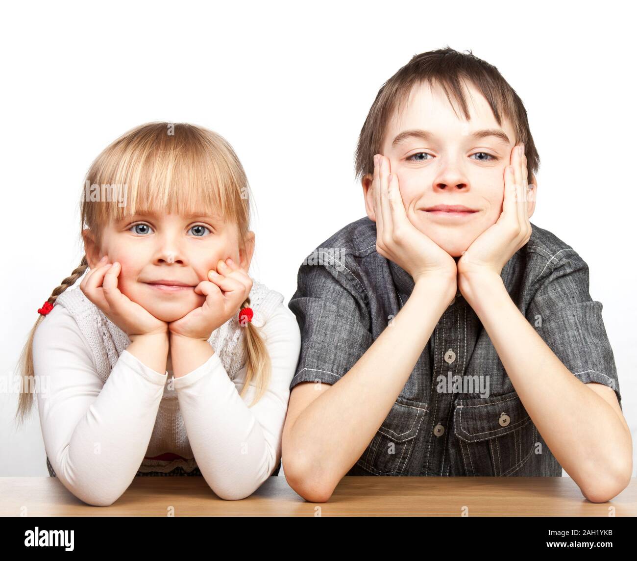 Portrait of cute girl and boy sitting at desk with hands on chin Banque D'Images