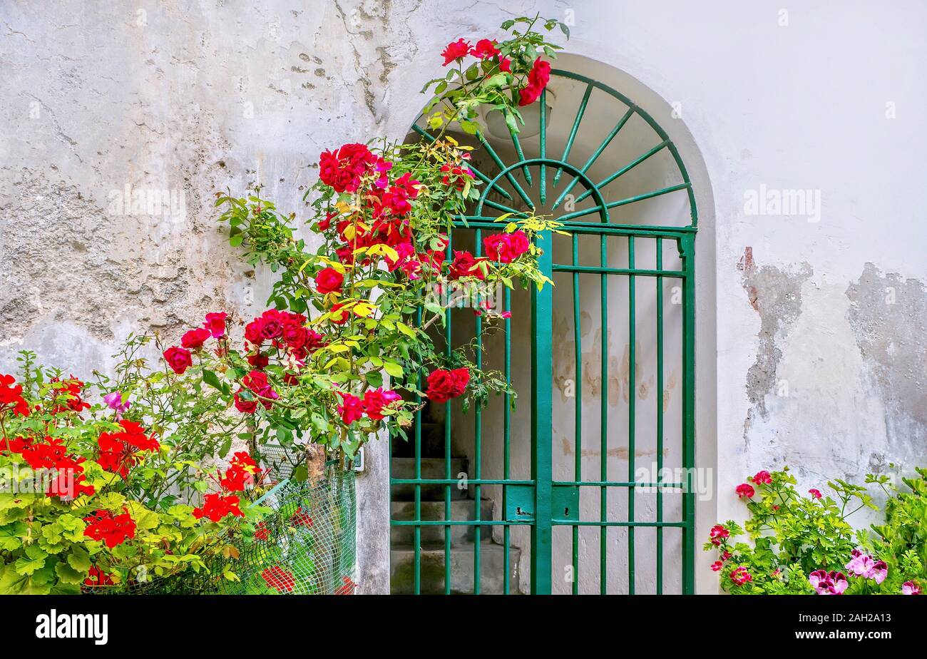 L'Été en Italie. Une vue sur la rue d'un édicule voûté avec une grille de fer, situé dans un vieux mur fissuré, avec un jardin d'ornement. Banque D'Images