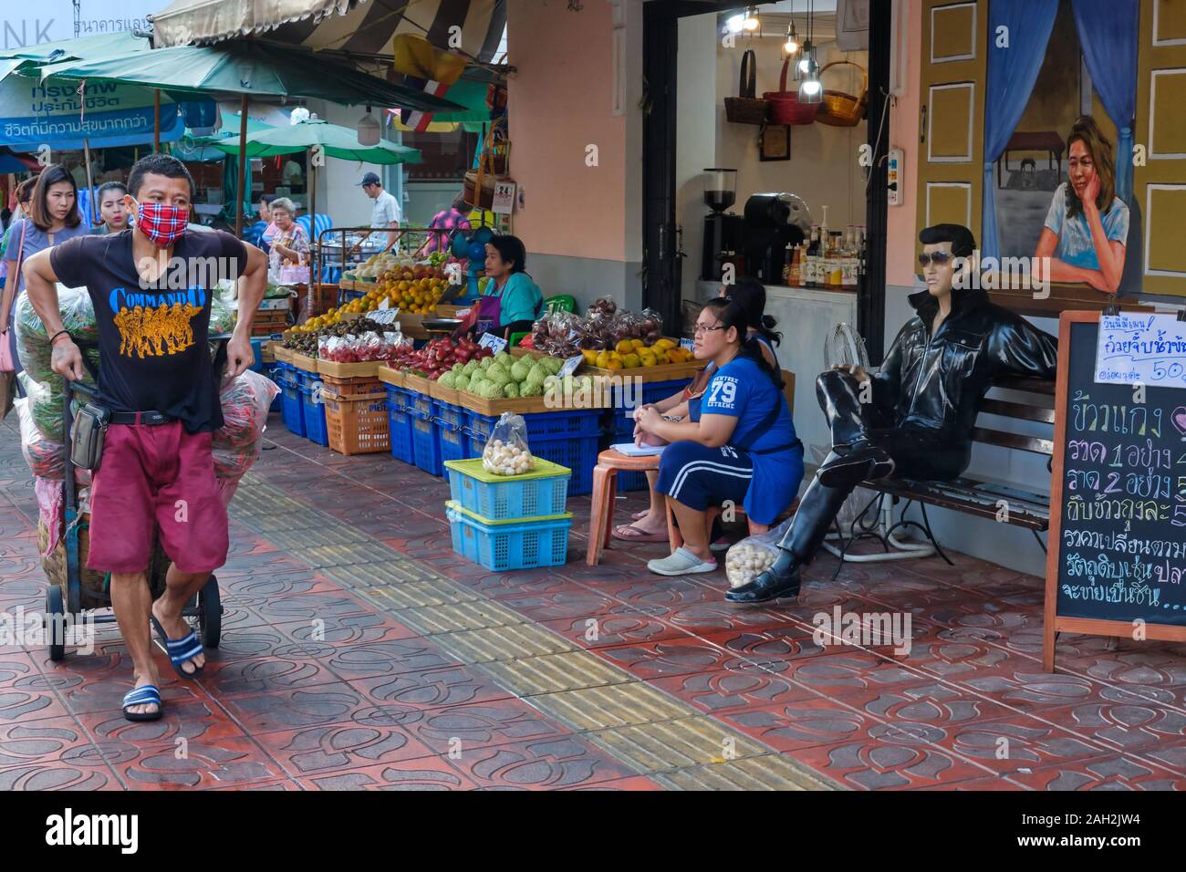 À Pak Klong Talaat (marché), à Bangkok, Thaïlande, un porteur tire un chariot devant une statue assise d'Elvis Presley, placée devant un petit café Banque D'Images