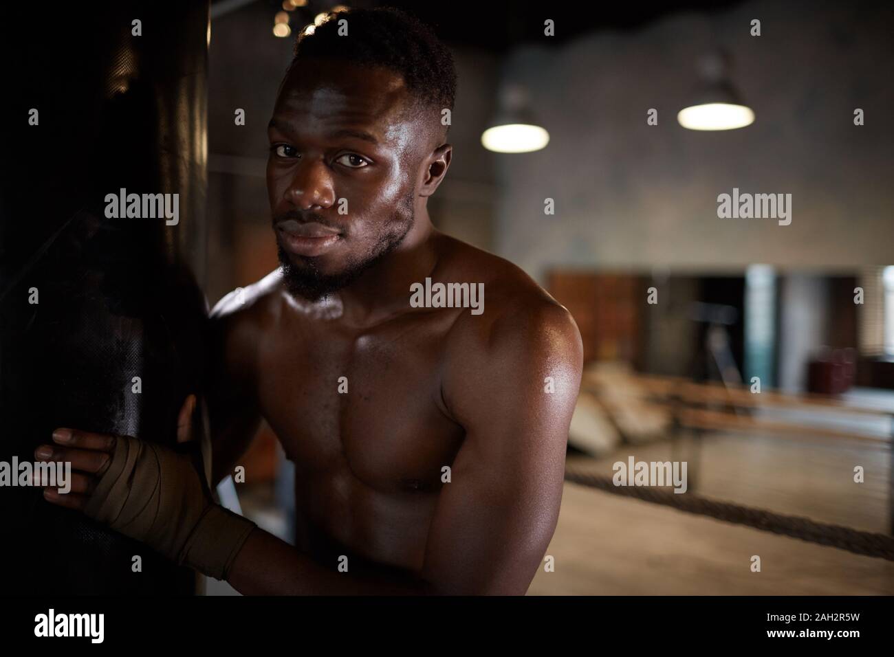 Portrait de l'homme torse nu, debout près de l'entraînement de sac de boxe et looking at camera in gym Banque D'Images
